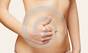 Woman is showing gesture thumb up in front of her abdomen