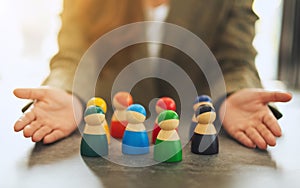 A woman showing a group of different colors wooden people toy in hands for diversity and business concept