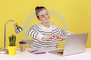 Woman showing heart gesture with hands to laptop screen sitting at workplace with laptop.