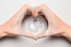 Woman showing heart gesture over paper cutout of family on light background, top view