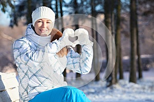 Woman showing heart shape with white mittens in sunlight at winter