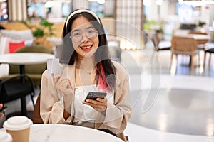 A woman is showing her credit card to the camera while sitting in a restaurant in a shopping mall