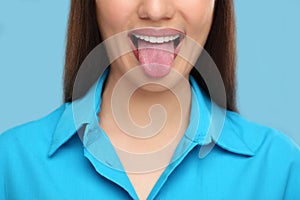 Woman showing her tongue on light blue background, closeup