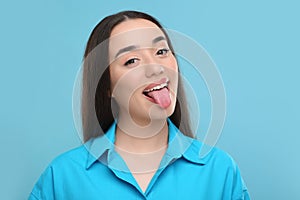 Happy woman showing her tongue on light blue background