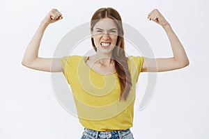 Woman showing how strong she is. Independent serious good-looking sportswoman in yellow t-shirt showing teeth frowning