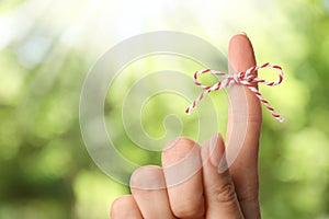 Woman showing index finger with tied bow as reminder on blurred green background, closeup