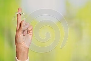 Woman showing index finger with tied bow as reminder on green blurred background, closeup. Space for text