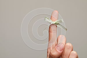 Woman showing index finger with tied bow as reminder on grey background, closeup. Space for text