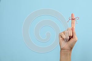 Woman showing index finger with tied bow as reminder on light blue background, closeup. Space for text