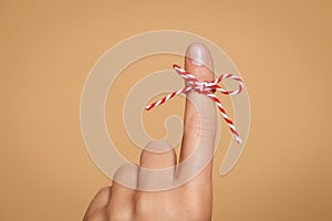 Woman showing index finger with tied bow as reminder on light brown background, closeup