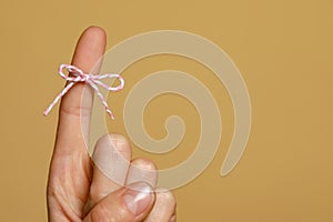 Woman showing index finger with tied bow as reminder on light brown background, closeup. Space for text