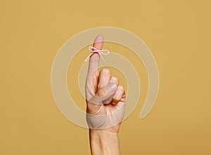 Woman showing index finger with tied bow as reminder on light brown background, closeup. Space for text