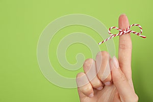 Woman showing index finger with tied bow as reminder on light green background, closeup. Space for text