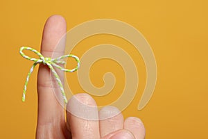 Woman showing index finger with tied bow as reminder on orange background, closeup. Space for text