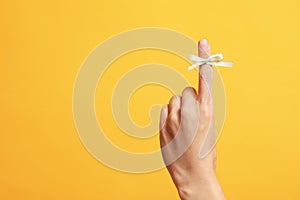 Woman showing index finger with tied bow as reminder on orange background, closeup. Space for text