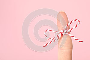 Woman showing index finger with tied bow as reminder on pink background, closeup. Space for text