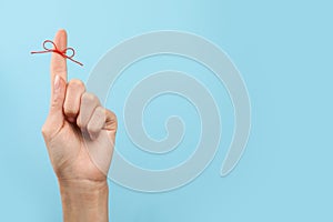 Woman showing index finger with tied red bow as reminder on light blue background, closeup. Space for text