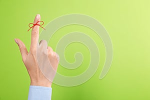 Woman showing index finger with tied red bow as reminder on light green background, closeup. Space for text