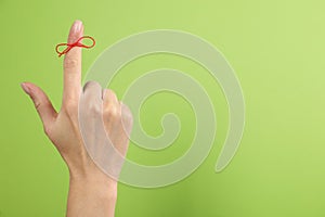 Woman showing index finger with tied red bow as reminder on light green background, closeup. Space for text