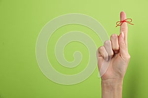 Woman showing index finger with tied red bow as reminder on light green background, closeup. Space for text