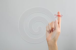 Woman showing index finger with tied red bow as reminder on light grey background, closeup. Space for text