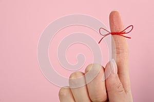 Woman showing index finger with tied red bow as reminder on pink background, closeup, Space for text