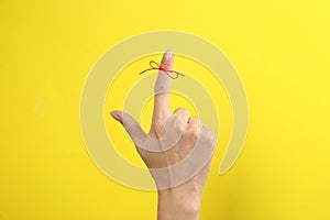 Woman showing index finger with tied red bow as reminder on yellow background, closeup