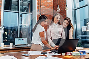 Woman showing the result of her work on laptop to colleagues standing in creative modern office