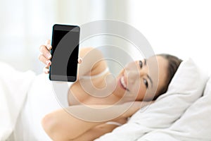 Woman showing a smart phone screen on the bed