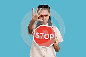 Woman showing stop gesture with hand and holding red stop sign board, enter is restricted.