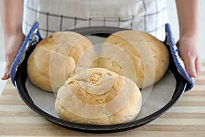 Woman showing three homemade loaves of bread in baking tray freshly baked