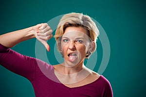 Woman showing thumb down gesture and tongue. People, lifestyle and emotions concept