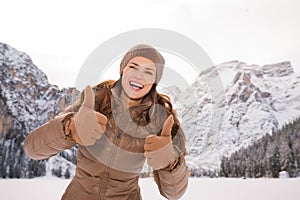 Woman showing thumbs up outdoors among snow-capped mountains