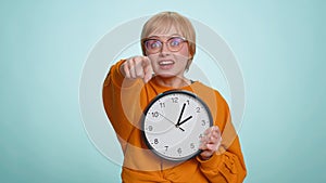 Woman showing time on wall office clock, ok, thumb up, approve, pointing finger at camera, your time