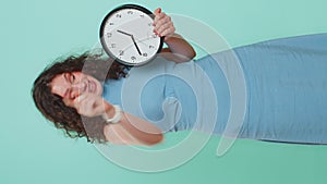 Woman showing time on wall office clock, ok, thumb up, approve, pointing finger at camera, your time