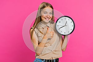 Woman showing time on wall office clock, ok, thumb up, approve, pointing finger at camera, your time