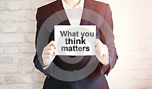 Woman showing white card with WHAT YOU THINK MATTERS word . Business