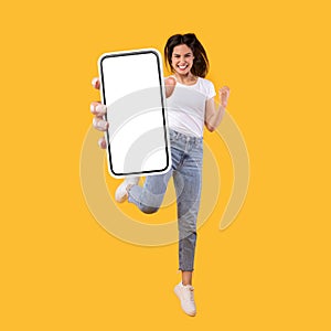 Woman showing white empty smartphone screen and jumping up