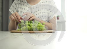 Woman showing wooden board with green grape, young woman eating grape footage