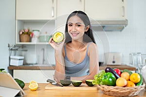 A woman shows an avocado to the camera while she prepares her healthy meals in the kitchen