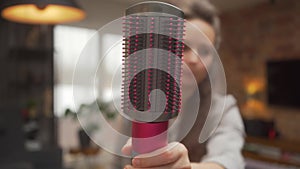 A woman shows a firm and soft brush for smoothing her hair with a hair dryer.