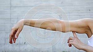 A woman shows the flabby muscles of the arm with her index finger.