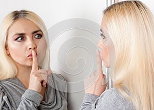 Woman shows silence sign looking at her reflection in the mirror