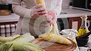 woman shucking shell hull fresh corn cob in her kitchen