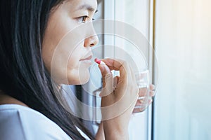 Woman sick with capsules putting in her mouth,female taking medicines and a glass of water,Concept for health photo