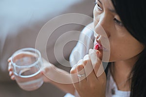 Woman sick with capsules putting in her mouth,female taking medicines and a glass of water