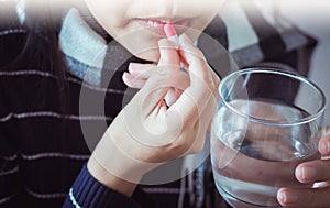 Woman sick with capsules putting in her mouth,female taking medicines and a glass of water photo