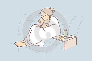 Woman sick with flu wrapped in blanket sits on couch and drinks hot decoction of herbs