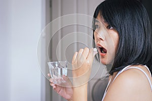 Woman sick with pill putting in her mouth,female taking medicines and a glass of water