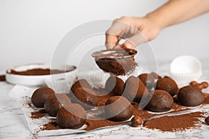 Woman sieving cocoa powder onto delicious chocolate truffles at white marble table, closeup